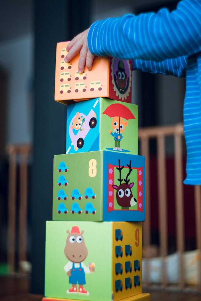 hero-img-02 A child playing indoors, stacking colorful wooden toy blocks with joyful illustrations.