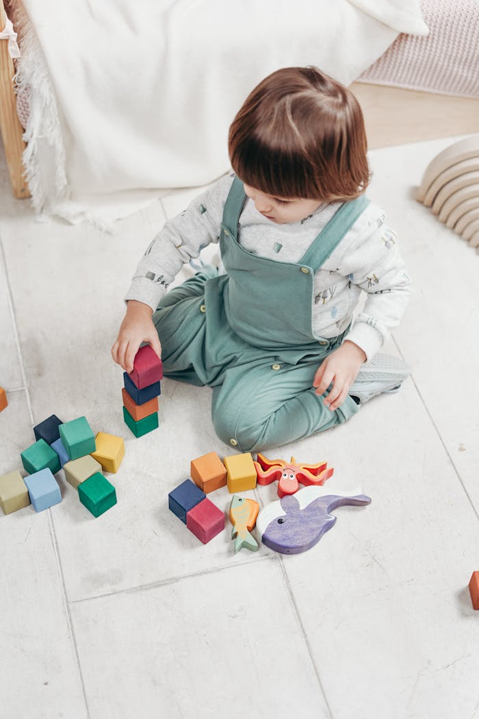 hero-img-01 A young child sitting indoors, playing with colorful wooden blocks and toys, focused on building.